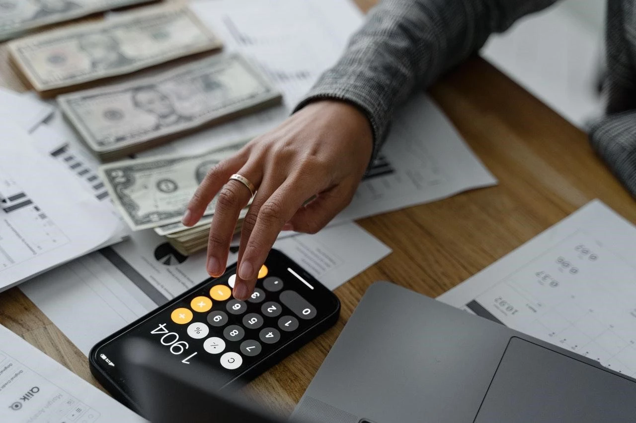 Person using a calculator on a desk with cash and paper