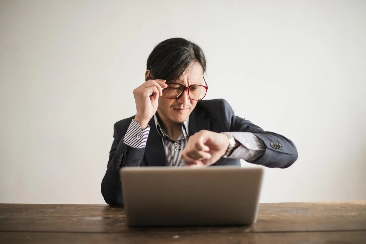 Man looking at watch in front of a laptop