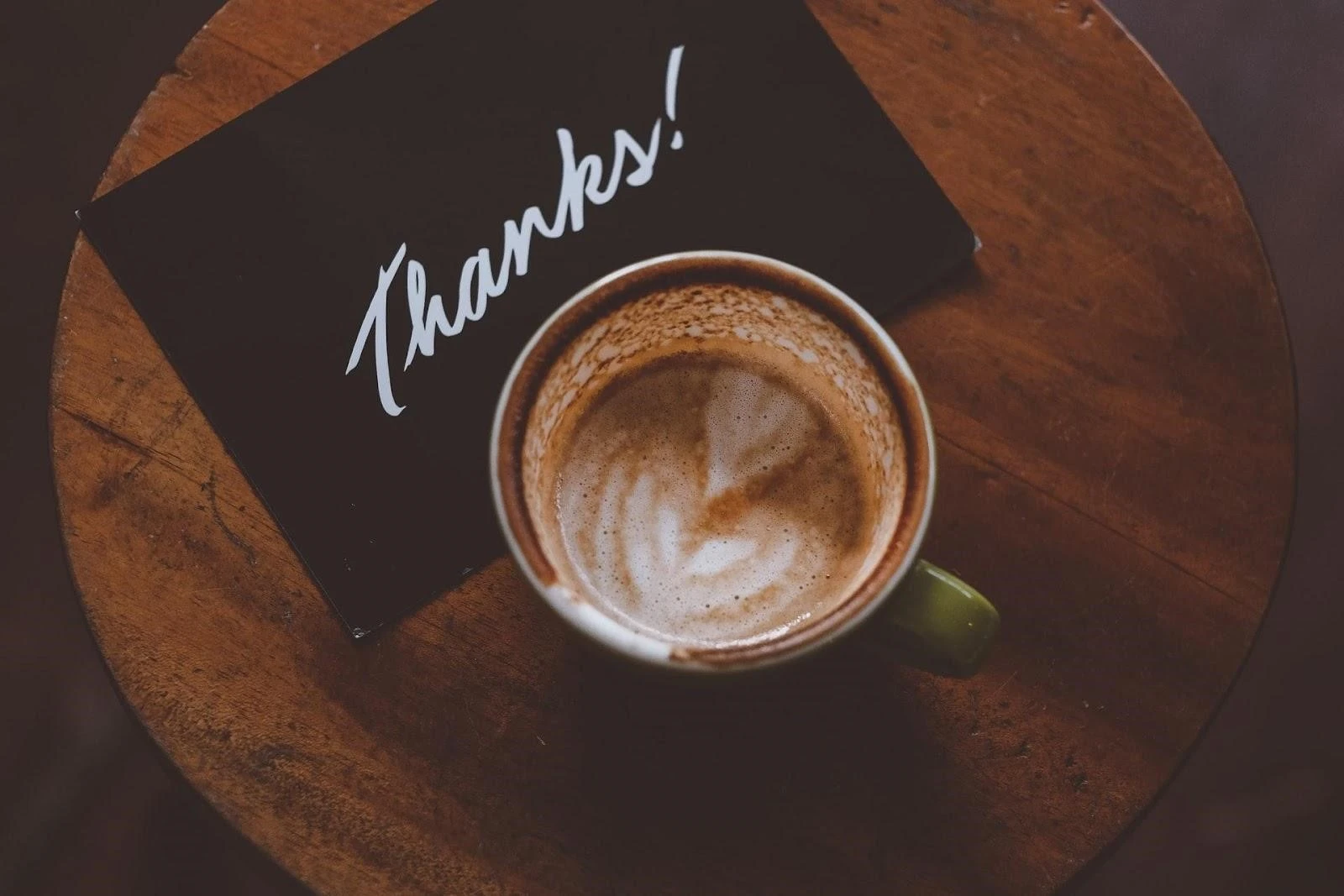 A cup of coffee with a thanks note on a table